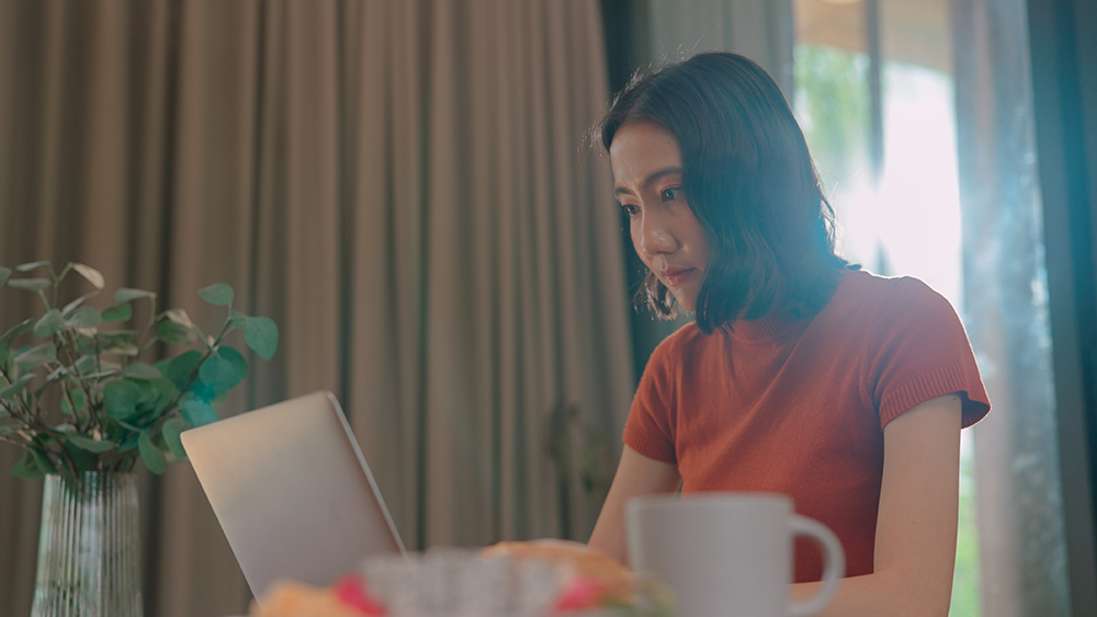 Woman calmly reviewing her laptop at a sunlit desk with a coffee cup and plant nearby